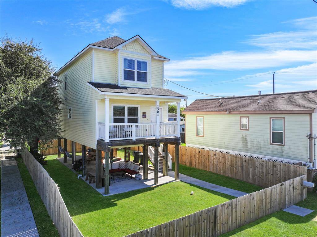 Elevated two-story home with a charming front porch, set on a fenced corner lot in the heart of Galveston features a covered outdoor area that's perfect for relaxation.
