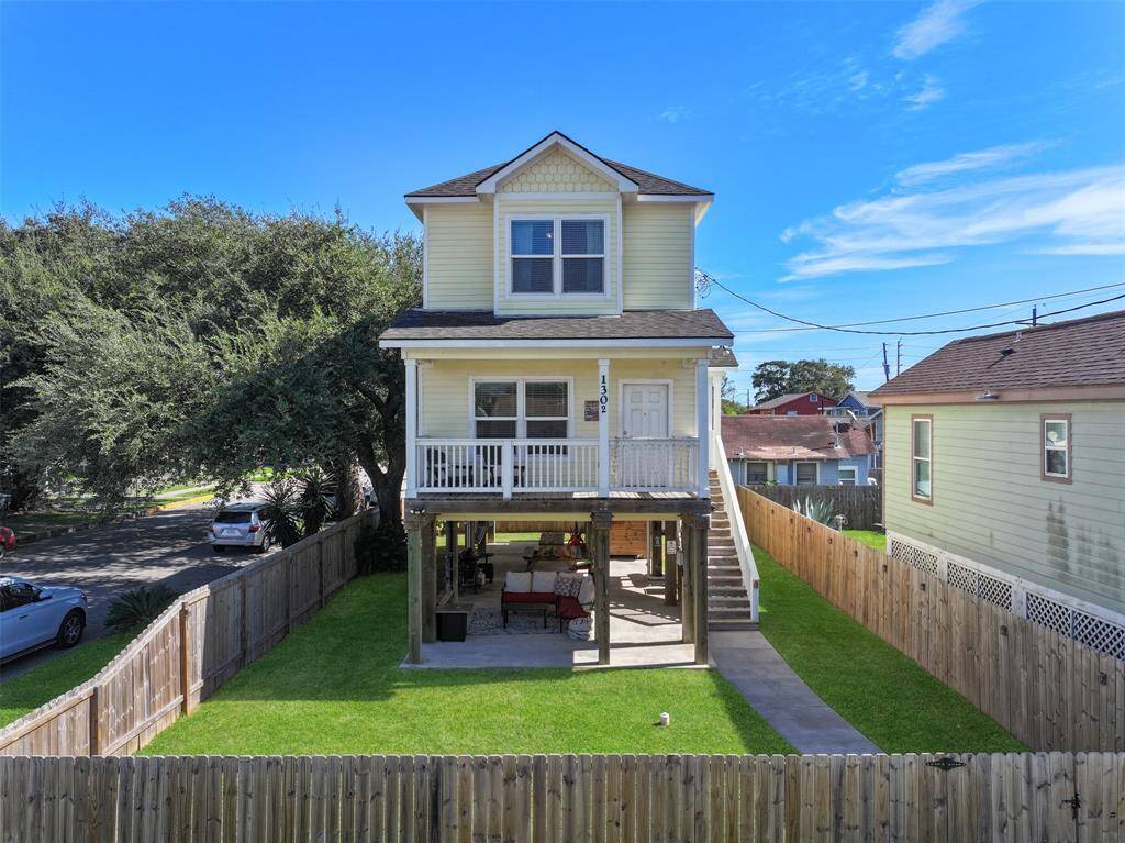 Elevated two-story home with a charming front porch, set on a fenced corner lot in the heart of Galveston features a covered outdoor area that's perfect for relaxation.