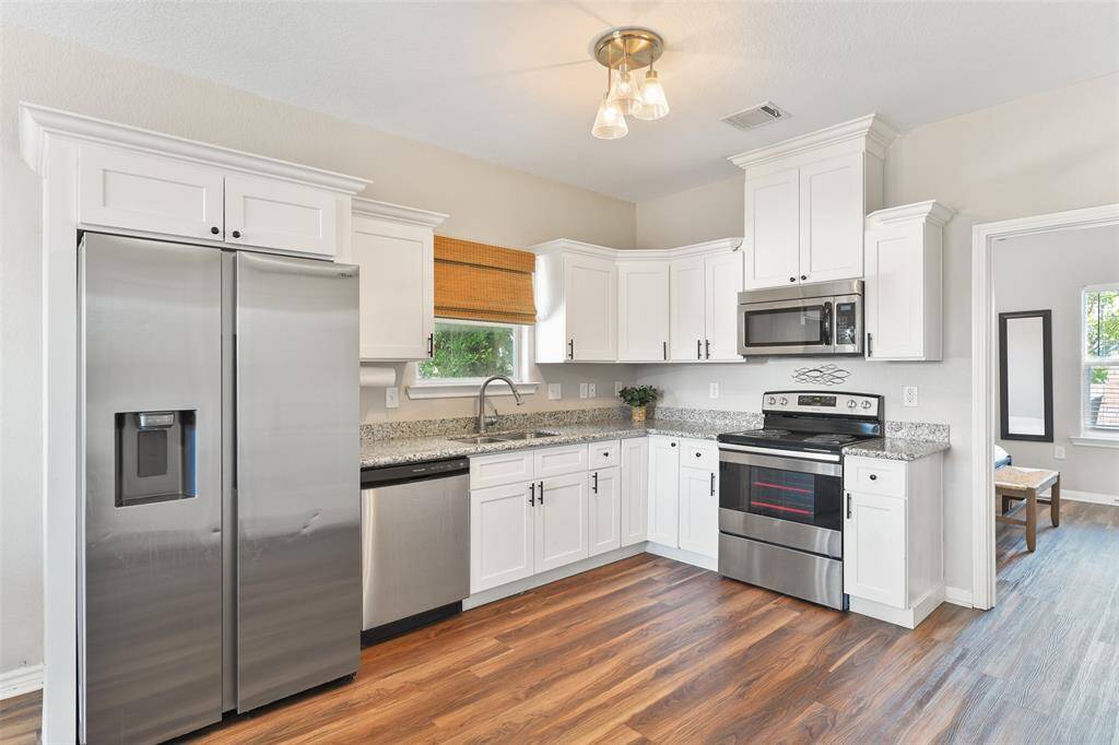 This kitchen features modern stainless steel appliances, granite countertops, and elegant white cabinetry. It offers ample storage space and a bright, inviting atmosphere with easy maintenance vinyl plank flooring and contemporary lighting.