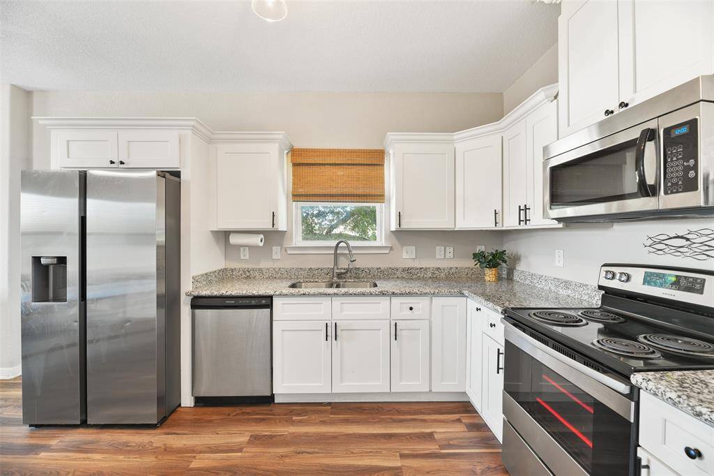 This kitchen features modern stainless steel appliances, granite countertops, and elegant white cabinetry. It offers ample storage space and a bright, inviting atmosphere with easy maintenance vinyl plank flooring and contemporary lighting.