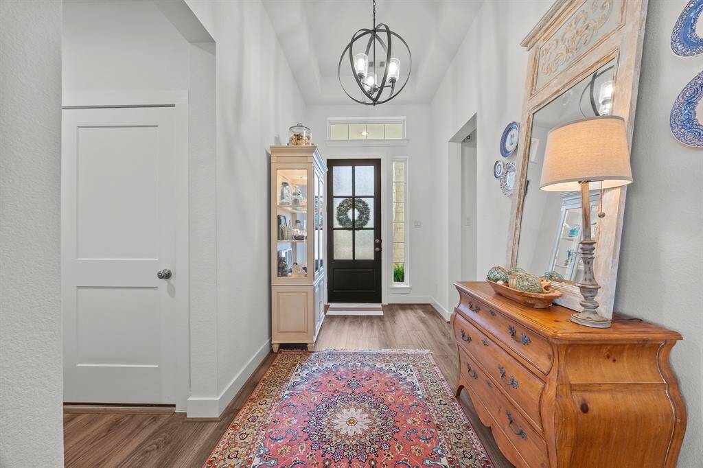Elegant foyer featuring soaring ceilings, luxury vinyl plank flooring, and a stunning light fixture complementing the stylish front door.