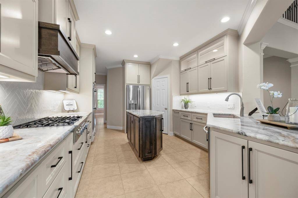The elegant kitchen features custom cabinetry, a central island, stainless steel appliances, and ample counter space. The open layout and cabinet lighting create a bright and inviting atmosphere.