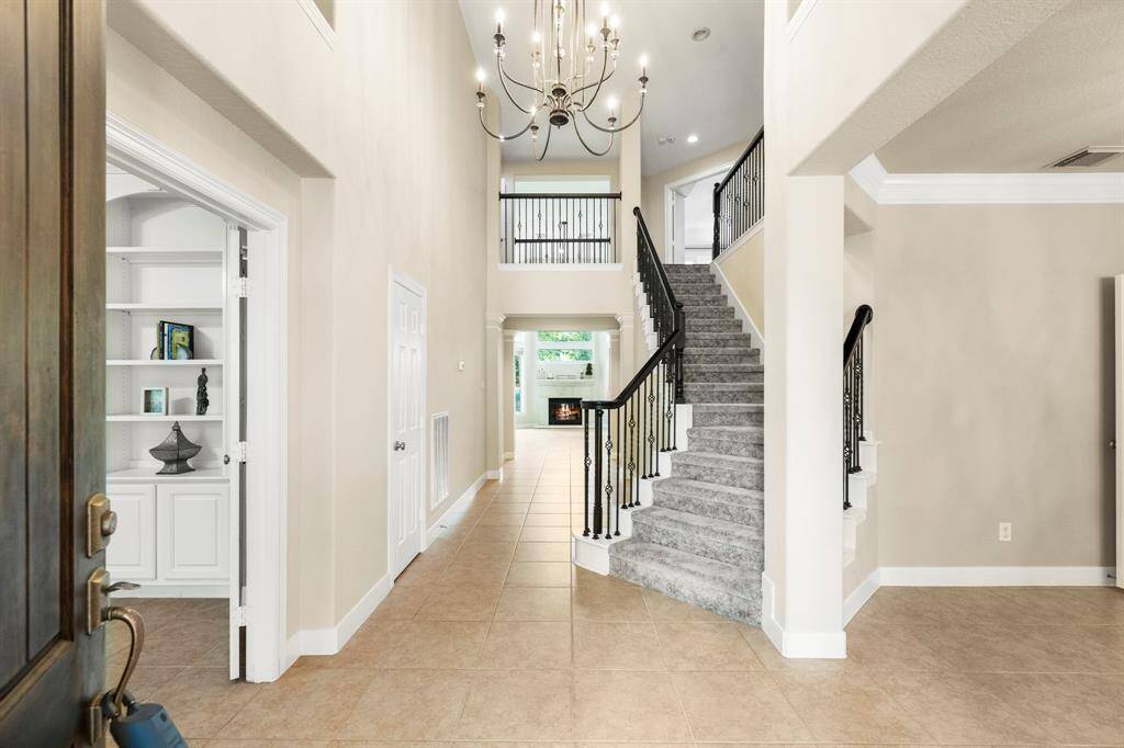 Spacious entryway with soaring ceilings. The open layout features a sweeping staircase with wrought iron railings leading to a light and bright living area.