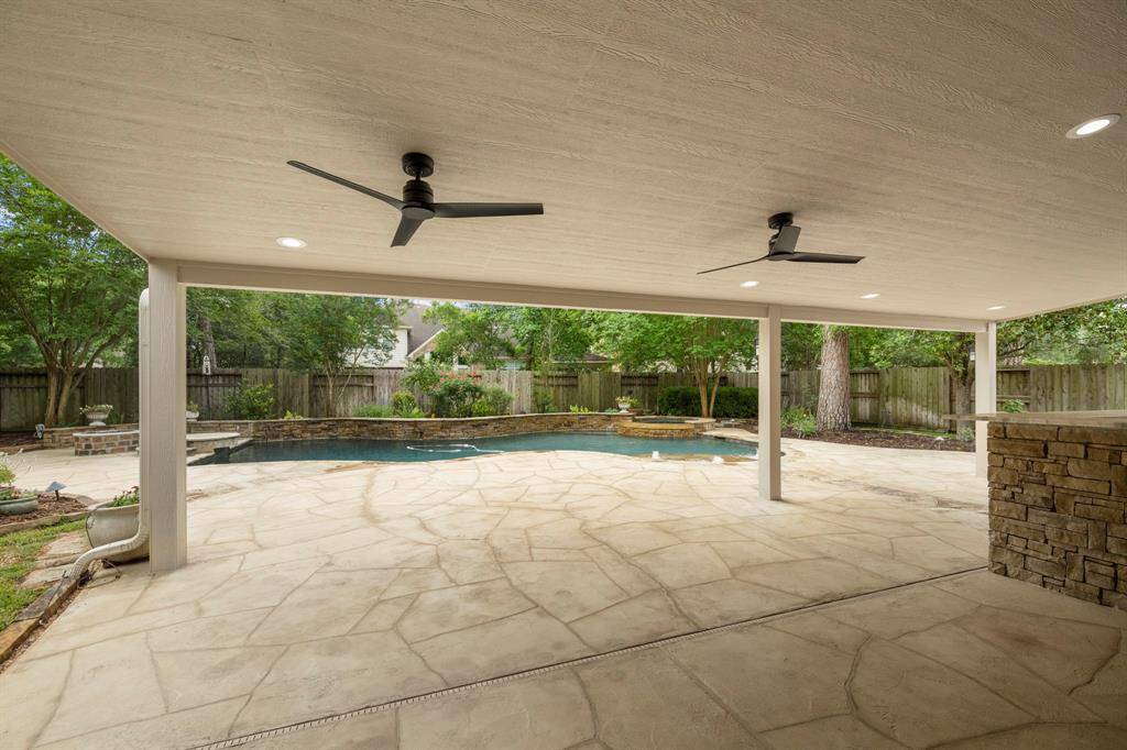 Expansive covered patio with ceiling fans overlooking the beautifully landscaped backyard and pool.