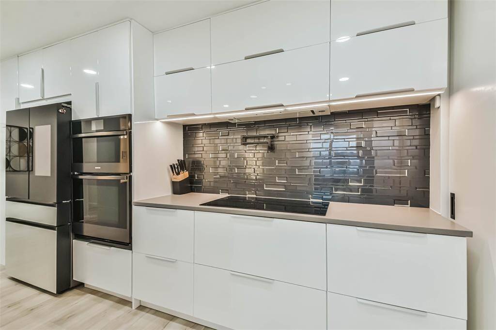 High gloss cabinets with soft close doors and drawers extend to the ceiling framing the glass tile backsplash with pot-filler.   Samsung smart appliances include induction cooktop and oven.  The microwave can be used as a second induction oven or air fryer.  The refrigerator/freezer includes beverage drawer and panels that can be changed out for different colors.