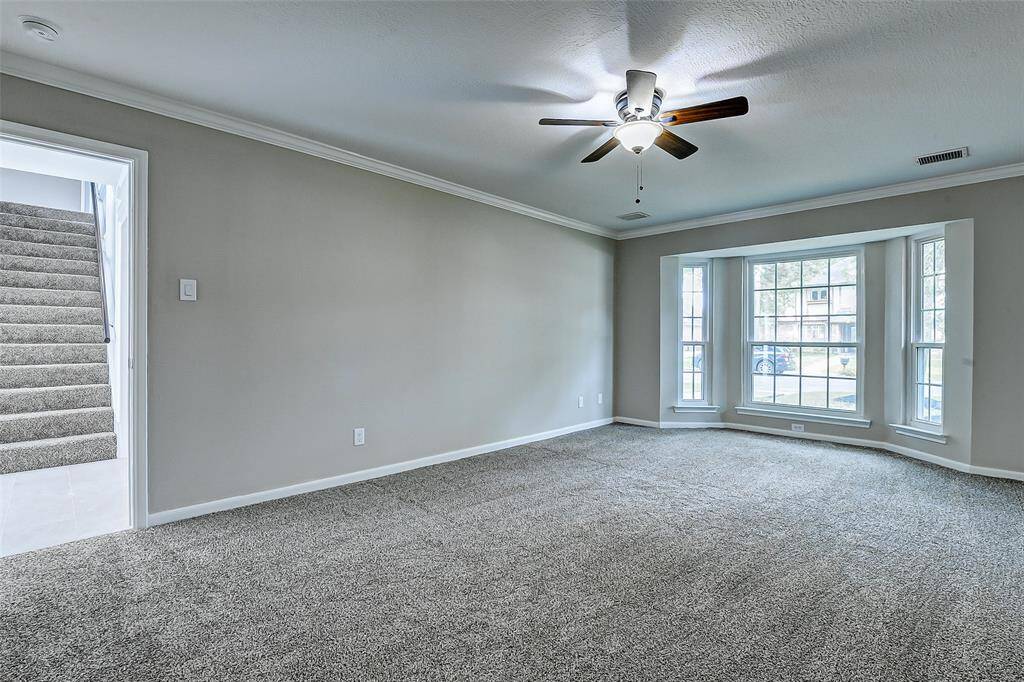 Large bay window allowing plenty of natural light, soft neutral walls, a new plush carpet, and a ceiling fan, creating a bright and welcoming atmosphere.