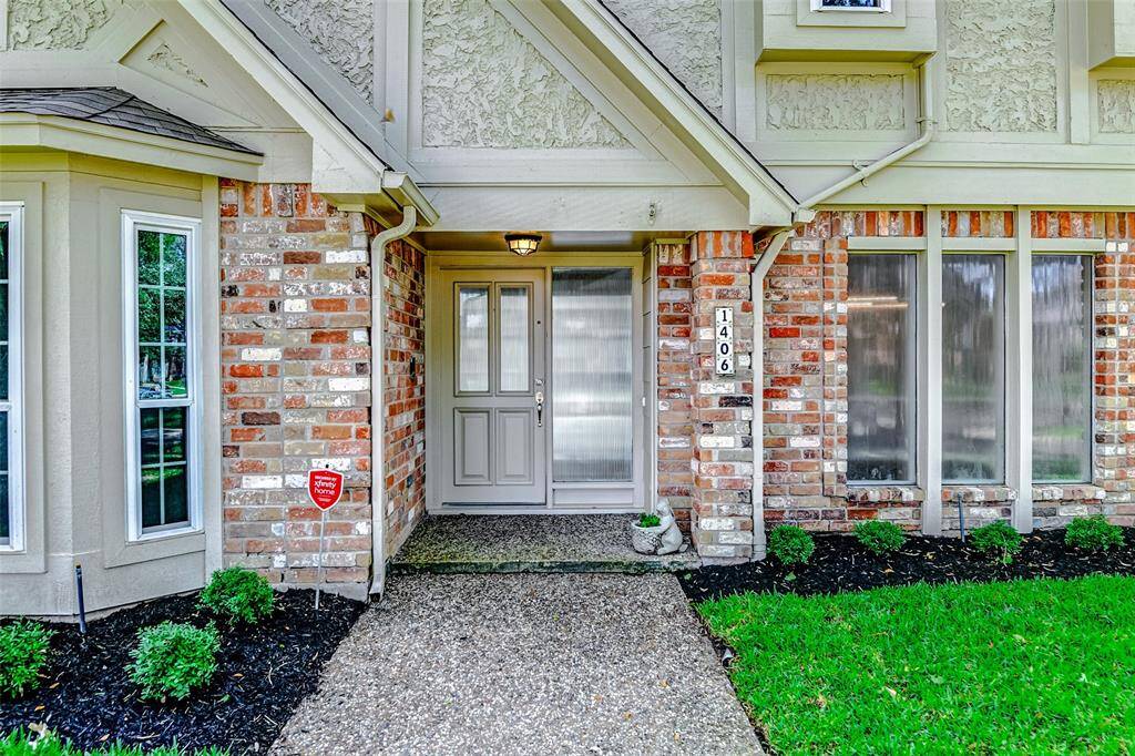 This welcoming entryway features a charming mix of brick and siding, a well-maintained pathway, and lush landscaping. The front door is complemented by large windows, providing a bright and inviting appearance.