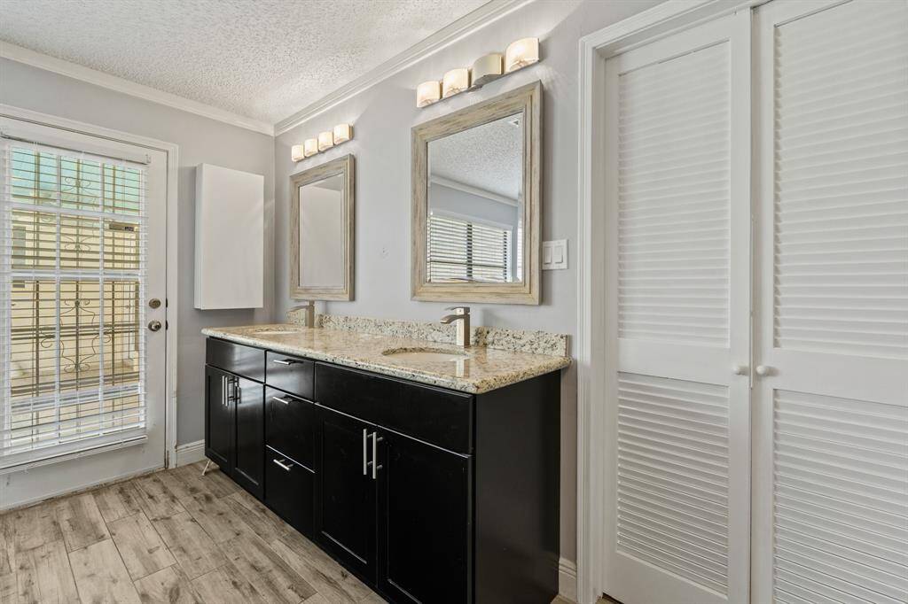 There are sleek contemporary cabinets with contrasting granite countertops and backsplash, double sinks, modern fixtures, framed mirrors, and a built-in closet.