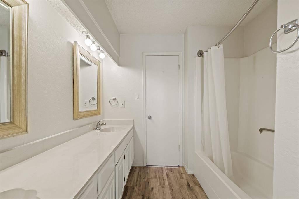 Secondary bathroom with framed mirrors, white cabinetry, double sinks, and a shower/tub combo.