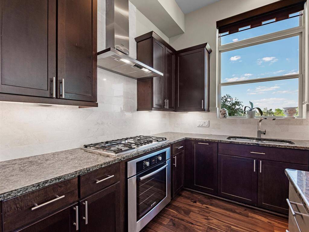 Well-appointed kitchen with rich dark wood cabinets, stainless steel appliances, and a gas cooktop. Granite countertops and a large window with scenic views create a bright, functional space filled with natural light.
