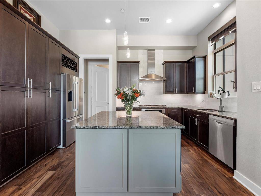 Kitchen offers dark wood cabinetry, stainless steel appliances, and a central island with granite countertops. Open-concept layout includes a bright window and modern light fixtures, blending function and style for everyday living and entertaining.