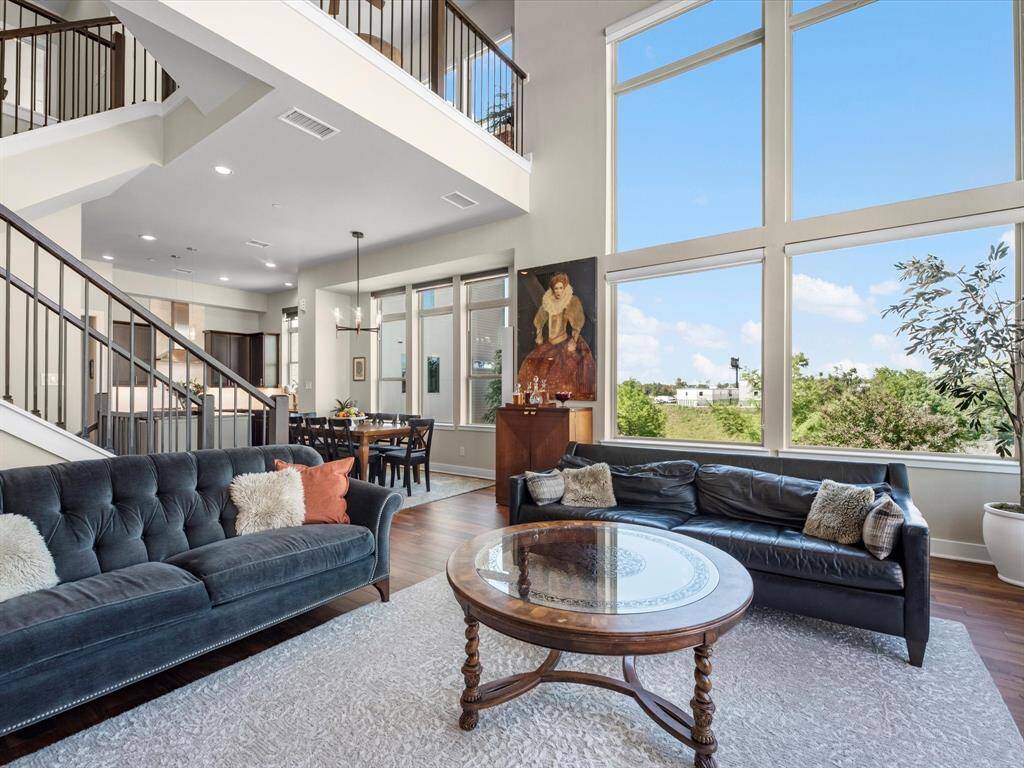 Open living area with high ceilings and wide windows that bring in soft natural light and views of the outdoors. The walnut floors flow through an easy layout that connects the living space to the kitchen and dining area—perfect for everyday living or hosting a get-together.