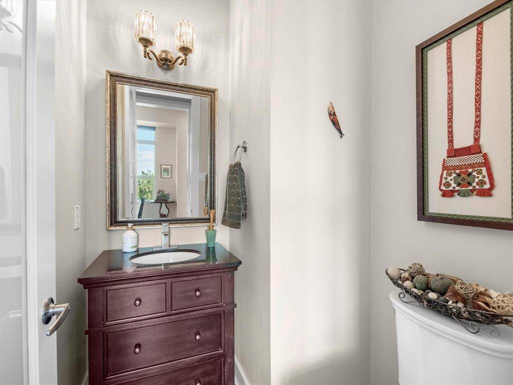 Bathroom features a dark wood vanity with sleek hardware, a large framed mirror, and updated light fixtures. Natural light brightens the space, complemented by soft wall tones and tasteful decorative accents for a clean, inviting feel.