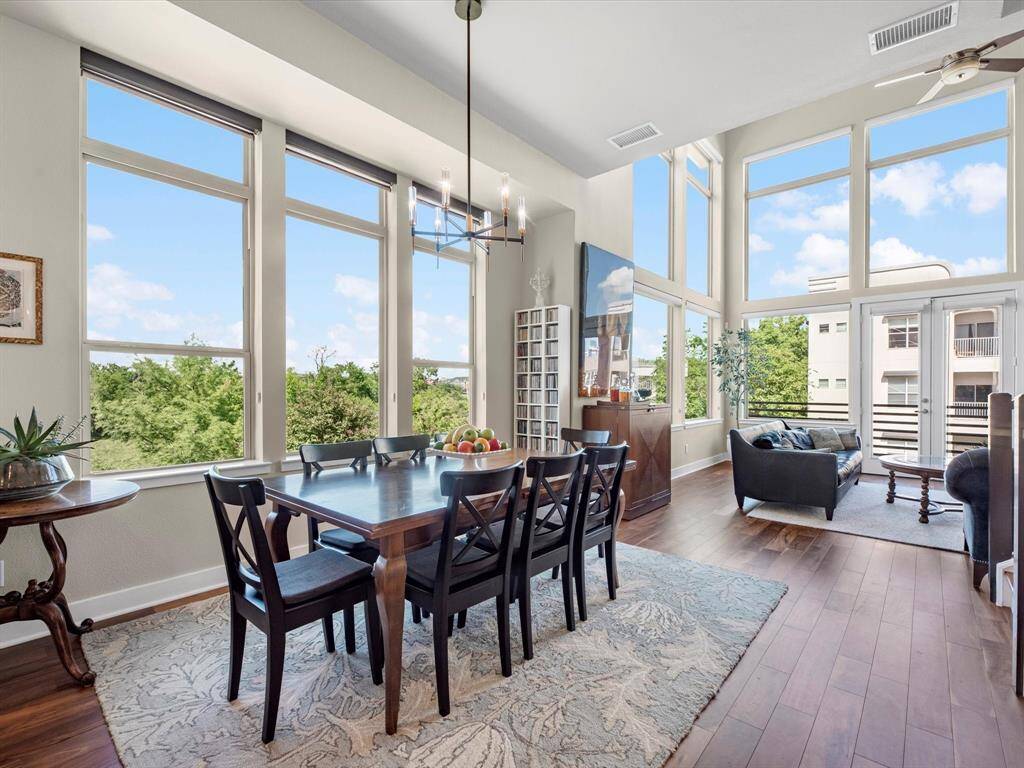 Living and dining area with large windows that bring in natural light and offer serene green views. Hardwood floors and high ceilings enhance the sense of space, creating a warm and welcoming setting for everyday living and entertaining.