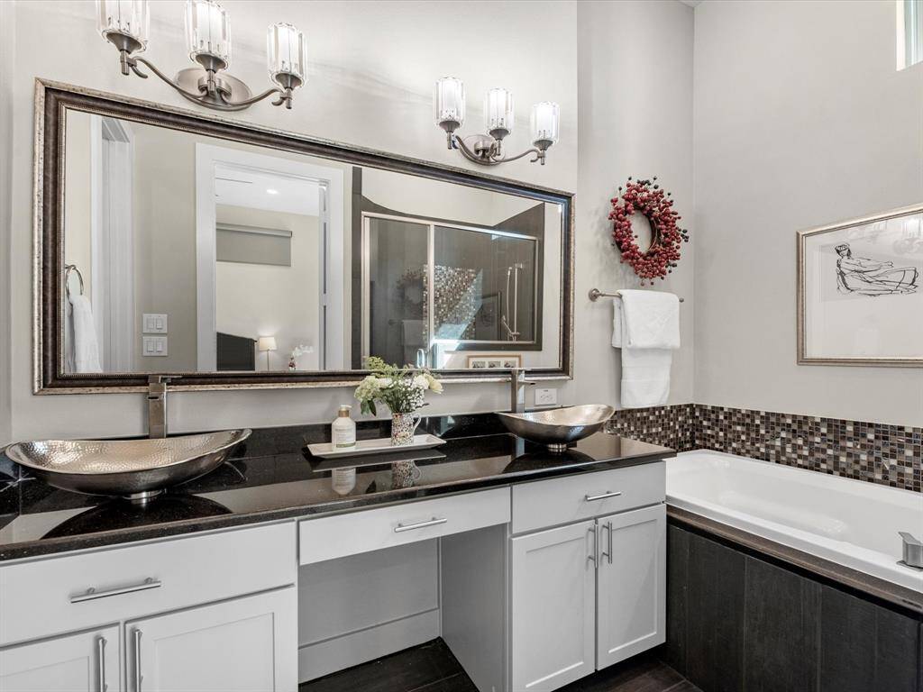 Bathroom with dual vessel sinks set on black countertops, complemented by a large framed mirror and contemporary lighting. A spacious tub with tile accents adds a touch of elegance, creating a refined and inviting atmosphere.