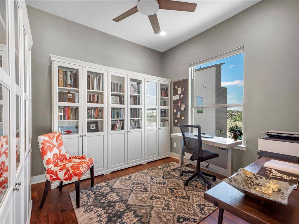 Home office features bookshelves with glass doors, a bright window for natural light, and with ample room for two desk setup. Creating an inviting workspace.
