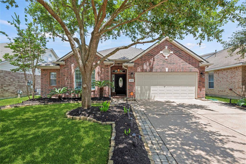 Charming single-story brick home featuring a well-manicured lawn with a mature tree, a two-car garage, and an inviting entryway.