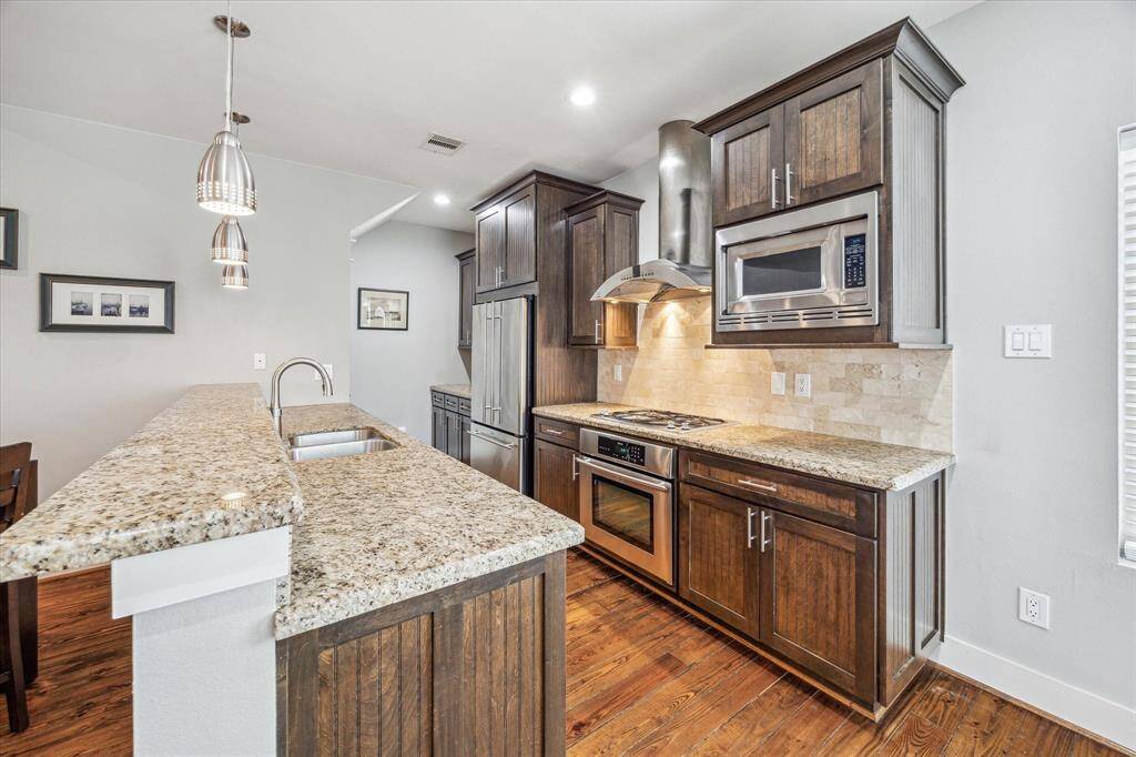 This kitchen features elegant granite countertops and rich wood cabinetry, complemented with stainless steel appliances. The open layout includes a breakfast bar and pendant lighting, creating an inviting and functional cooking space.