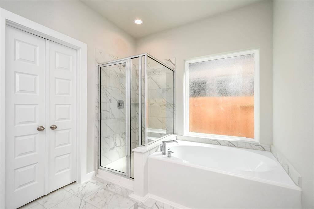 Escape to a spa-like oasis in this primary bathroom. Enjoy a walk-in shower with tile surround, a separate garden tub with custom detailing, and an elegant vanity featuring light countertops, modern hardware, and beautiful recessed lighting. Experience luxury and relaxation in every detail. Sample photo of completed home with similar floor plan. Actual colors and selections may vary.