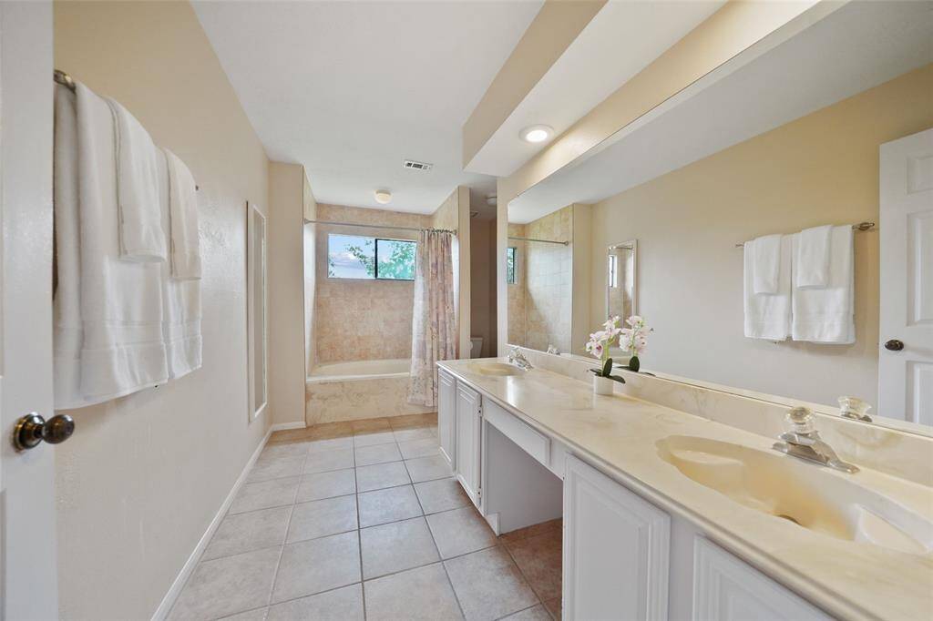 Luxurious primary bathroom featuring a spacious double vanity, elegant tile flooring, and a relaxing tub with a view.