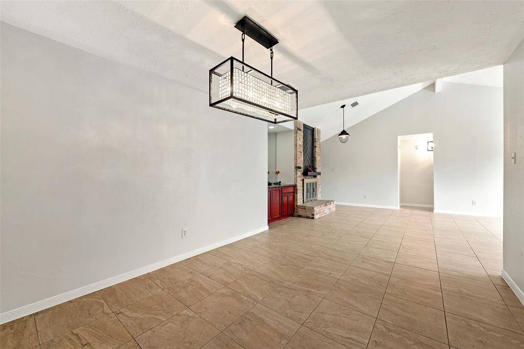 Bright and spacious dining area with a modern light fixture, next to a wet bar and fireplace.
