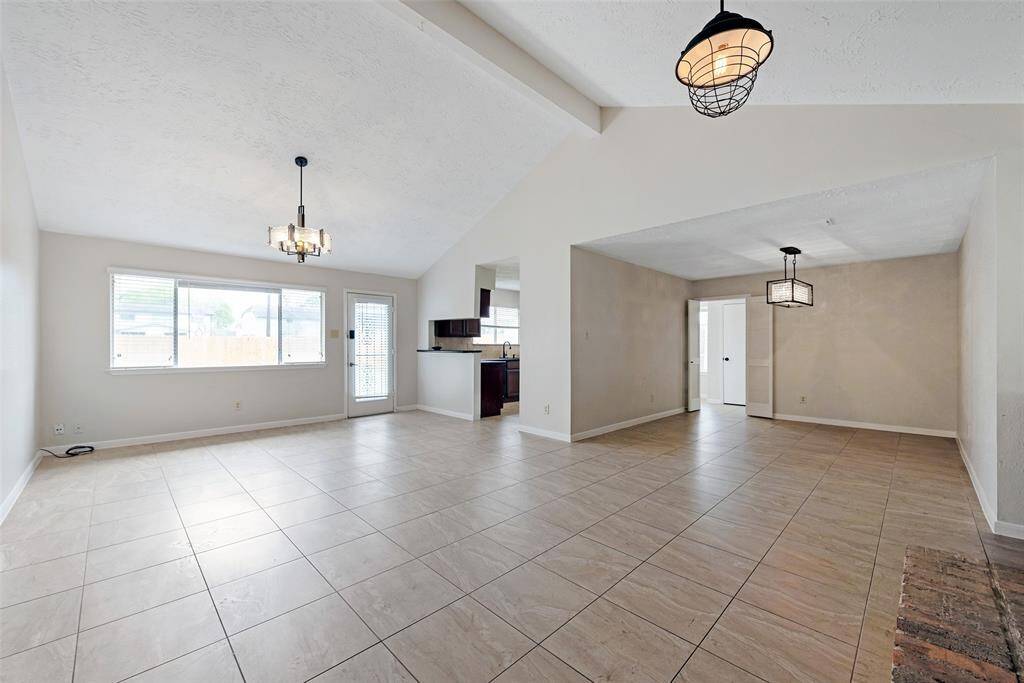 This spacious living area features high ceilings, neutral tile flooring, and ample natural light from large windows and a glass door. Modern light fixtures add a stylish touch. Perfect for comfortable living and entertaining.