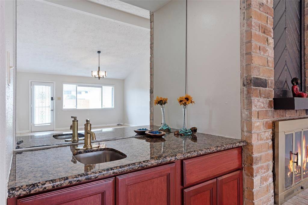 This photo showcases a wet bar with premium granite countertop, warm custom built wooden cabinetry, and a charming brick fireplace.