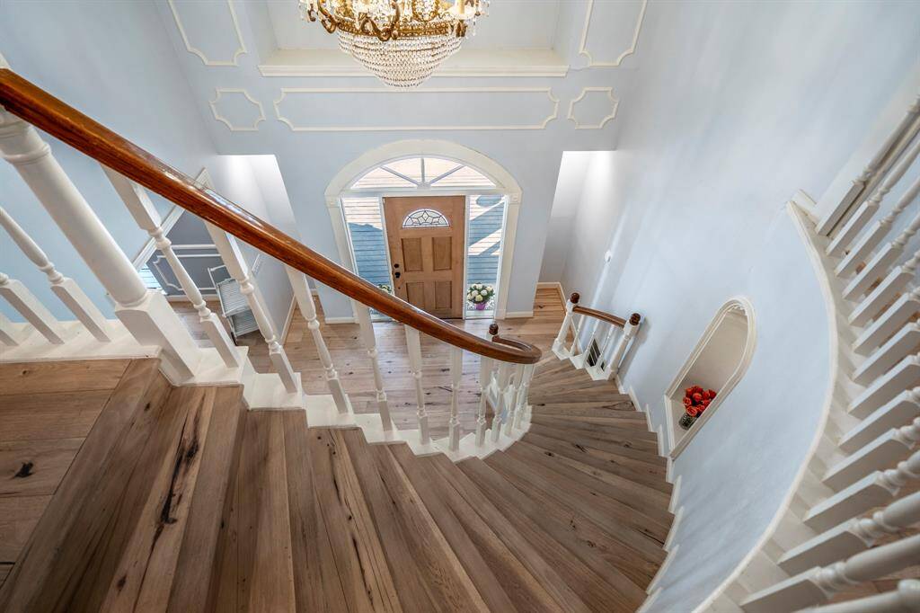 The elegant dining room features a large arched window, a classic chandelier, and light hardwood flooring. With soft gray walls and white wainscoting, it offers a bright, inviting space perfect for gatherings.