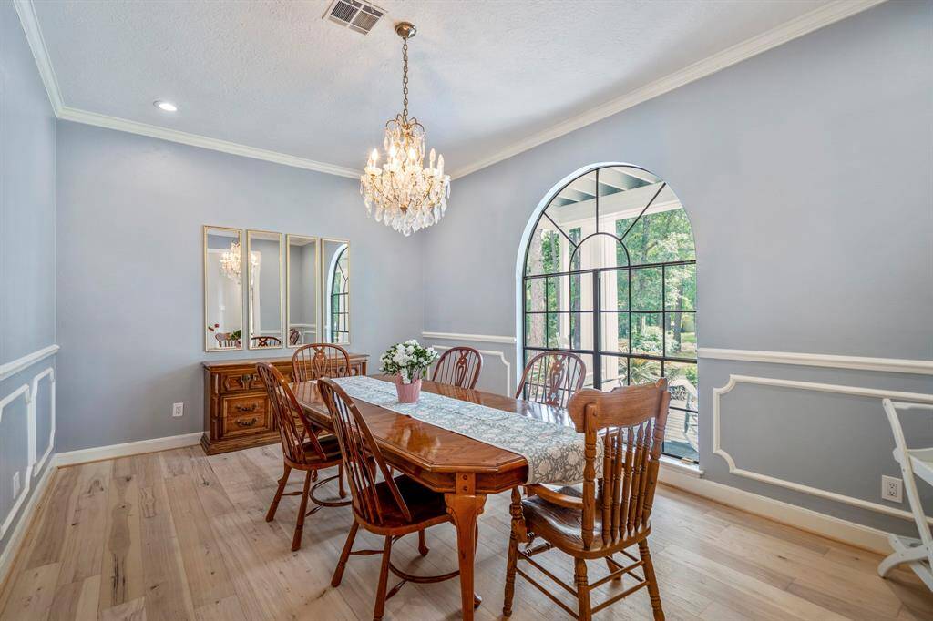 This spacious living room features large arched windows with views of a lush garden and pool, allowing for abundant natural light. It has elegant light fixtures, a cozy fireplace, and plush blue seating, creating a luxurious and inviting atmosphere.