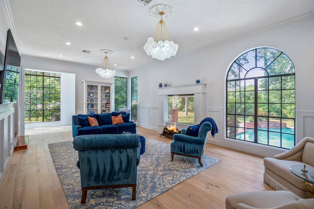 Bright living room with room for a large TV. Features a modern chandelier, wood flooring, and wainscoting. French doors open to a charming sunlit room with wooden accents.