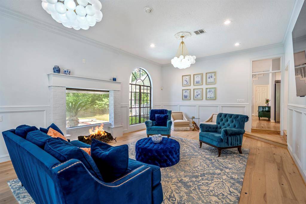 The study features elegant wood paneling, a large arched window with garden views, and warm hardwood floors. It includes a cozy sitting area creating a sophisticated and inviting space.