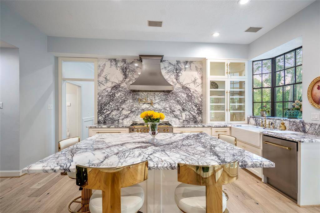 This kitchen features elegant marble countertops and backsplash,  and large windows offering plenty of natural light. The open layout leads to a deck with recently installed doors creating a seamless indoor-outdoor flow.