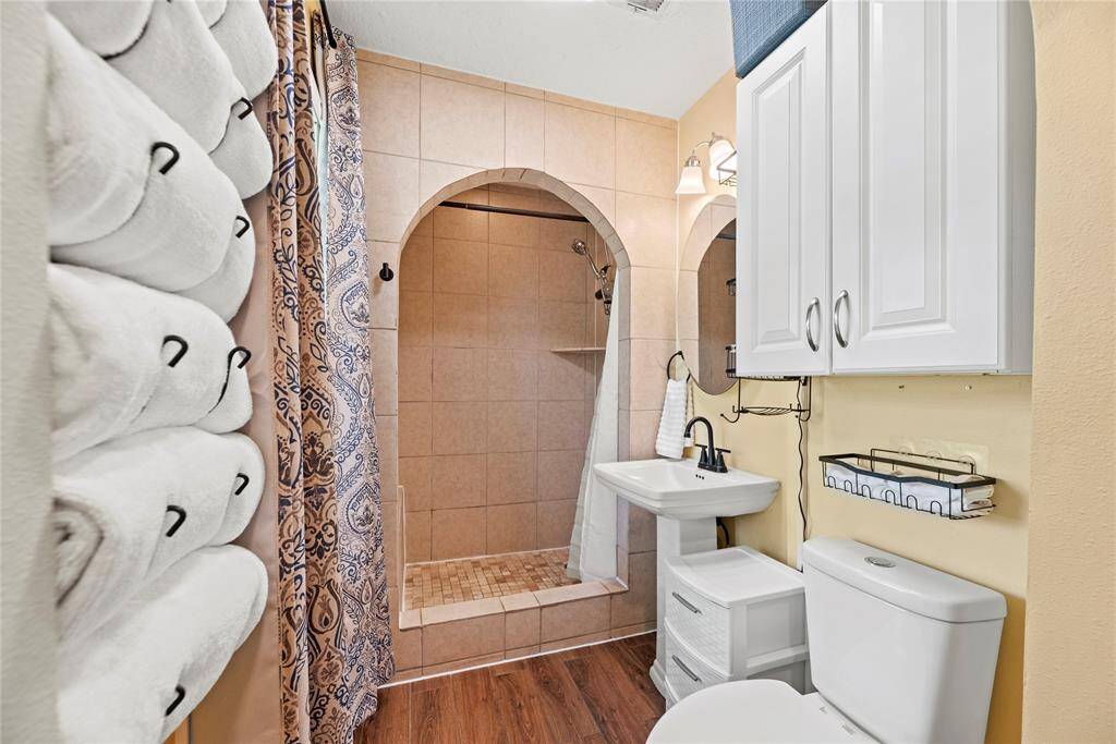 Enjoy a spacious walk-in tiled shower with arched entry, pedestal sink, and built-in storage, combining comfort and convenience.