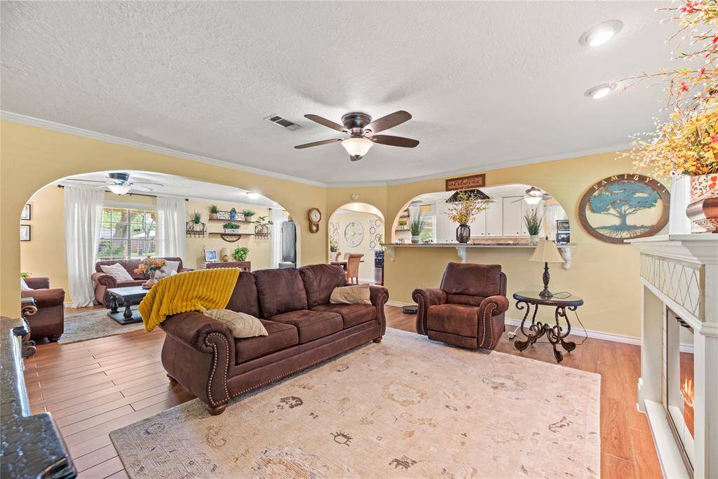 Spacious and inviting, this open-concept living and dining area is perfect for gatherings and everyday comfort. Featuring wood-look flooring, soft archways, and elegant crown molding, the space is anchored by a cozy fireplace and large windows that fill the room with natural light.