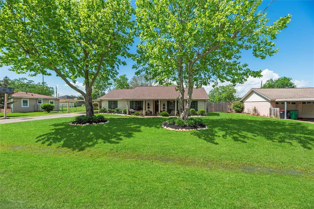 Another angle of the beautifully maintained front yard highlighting the spacious lot, lush greenery, and symmetrical tree framing.