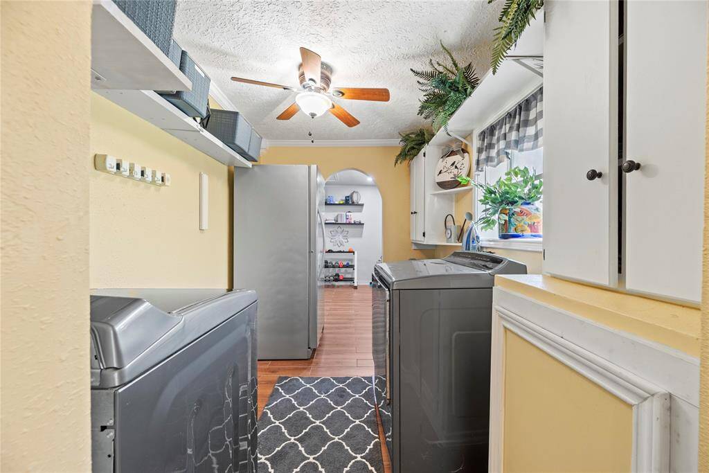 Functional laundry room with upper cabinets, open shelving, and natural light from a large window.