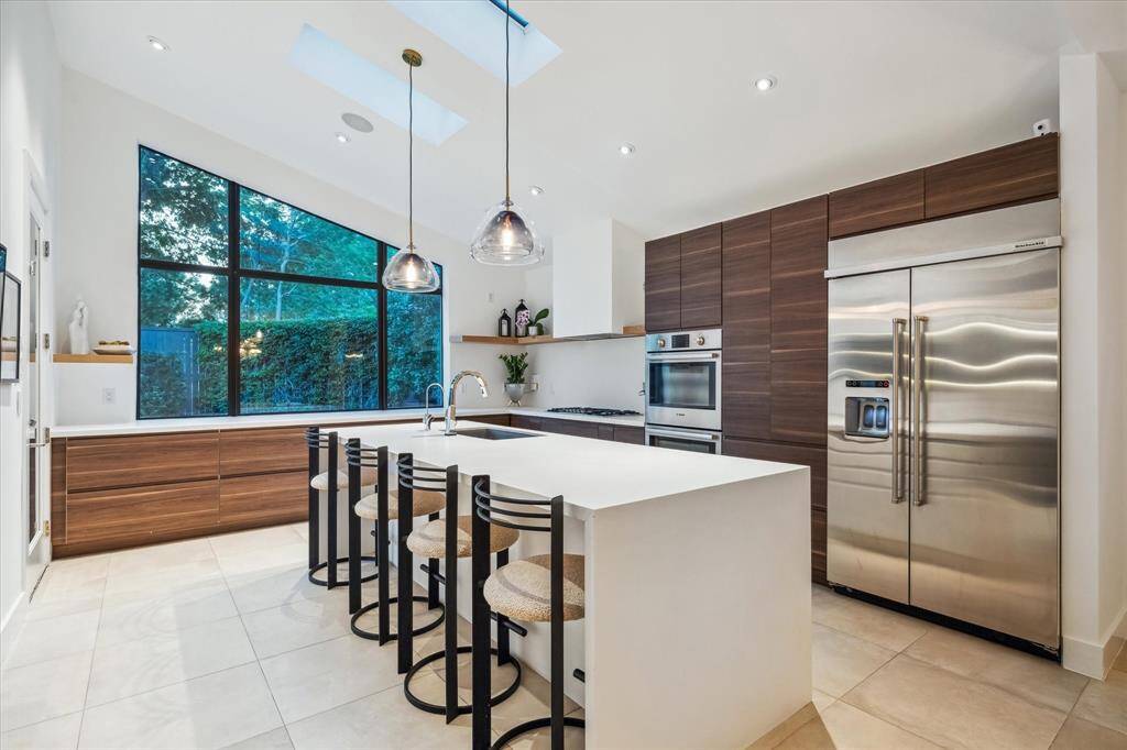 Bathed in natural light from skylights and a dramatic picture window, this chef's kitchen boasts rich wood cabinetry with interior lighting, premium appliances, and a generous island perfect for entertaining.