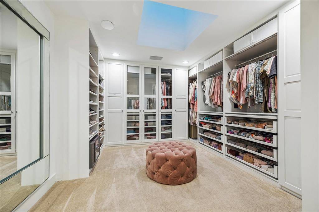 The expansive primary closet doubles as a chic dressing room, featuring custom built-ins with clear-front drawers for easy organization, LED lights, and a skylight that floods the space with natural light. It also has direct access to the laundry room.