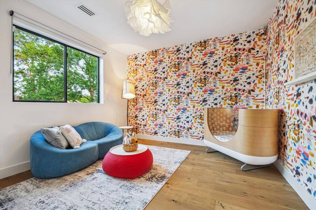 This spacious, secondary bedroom features designer Pierre Frey wallcovering and a delicate and playful light fixture.