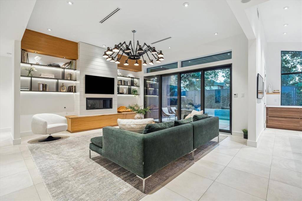 This stunning modern living room features sleek white oak shelving, a cozy fireplace, floor-to-ceiling sliding glass doors that fully open, providing a seamless indoor-outdoor flow to a private backyard oasis.