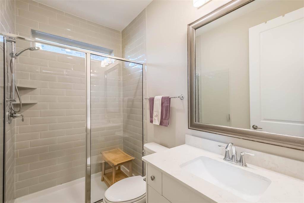 The guest suite bathroom features a large walk-in shower with window, quartz counters and framed mirror.