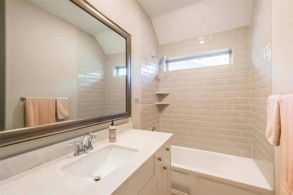 Upstairs secondary bathroom with tub/shower combo, window, quartz counters and a framed mirror.