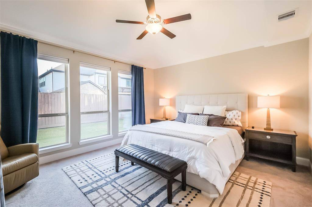 The primary suite is spacious and bright with oversized windows and a ceiling fan.
