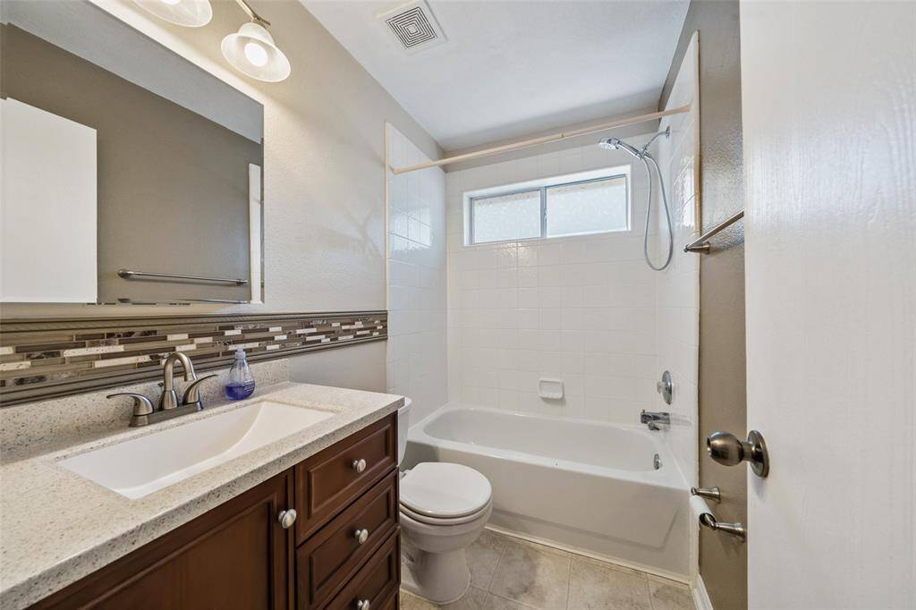 The guest bathroom offers a sleek single sink vanity with a full mirror and vanity lights above plus a convenient fully tiled tub/shower enclosure.