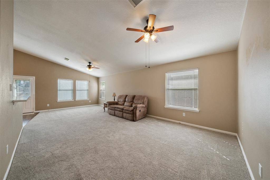 Gather with ease in this expansive family room featuring plush carpet, a vaulted ceiling, and neutral paint. Oversized windows bring in natural light, while the open layout flows seamlessly into the dining area and kitchen, ideal for entertaining or enjoying a quiet evening in.