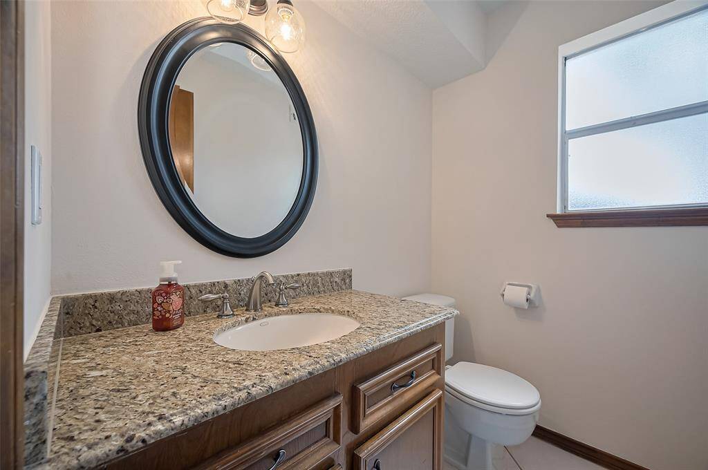 The updated half-bathroom features a granite vanity with an undermount sink, complemented by a round mirror and updated overhead lighting. A frosted window provides privacy while allowing natural light. Conveniently located near the back doors, this bathroom offers easy access for children coming in from the backyard and provides a private, guest-friendly space—not tucked away in the utility room with laundry.