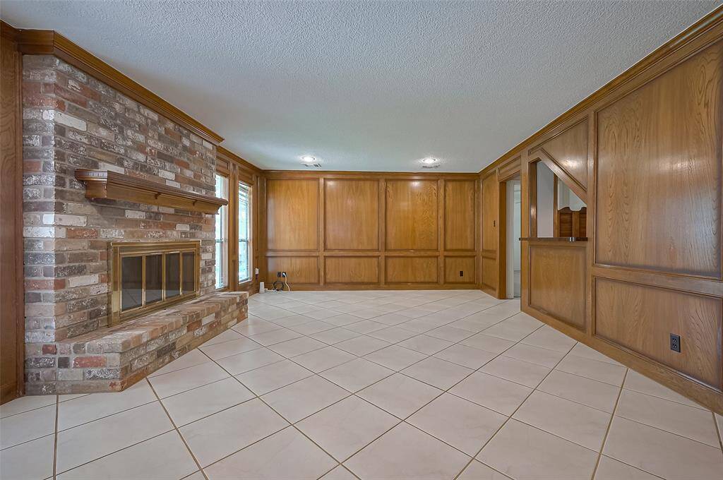 The floor-to-ceiling brick fireplace is a striking focal point, complete with a classic brick hearth and wood mantle. Designed for versatility, it can be enjoyed as a wood-burning or gas log fireplace—currently outfitted with ceramic gas logs for cozy evenings and easy turn-off convenience. Framed by large windows on either side, the space is bathed in natural light and offers a clear view of the backyard—perfect for keeping an eye on little ones at play while enjoying the comfort and ambiance indoors.