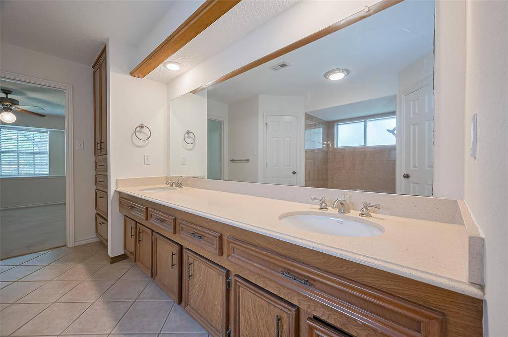The ensuite bathroom features a granite vanity with two undermount sinks, offering separate space for busy mornings. Two operable drawers between the sinks and ample lower cabinets provide great storage. A full wall mirror and recessed LED lighting brighten the space. At the far end, a built-in linen closet with upper cabinetry and four drawers adds even more convenient storage—because who doesn’t appreciate cherished storage in a bathroom?