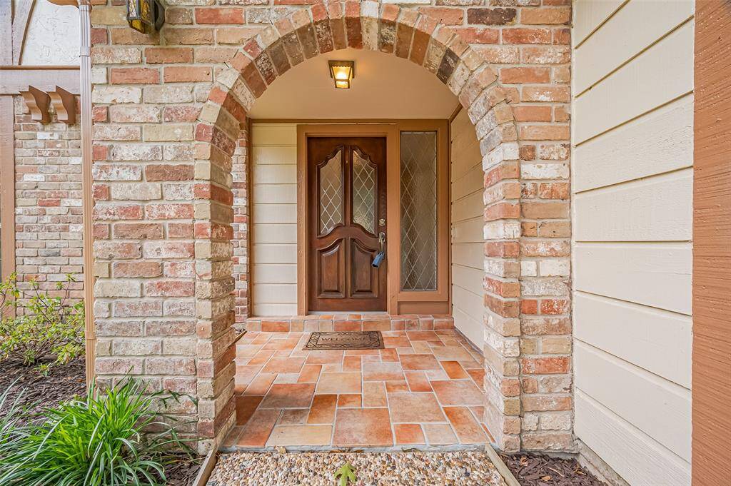 Pea gravel walkway leads to a covered front entry with arched opening and tiled porch. Features a beautifully polished leaded glass door with matching side-light window. Warm and inviting, the covered entry is perfect for welcoming guests, rain or shine.