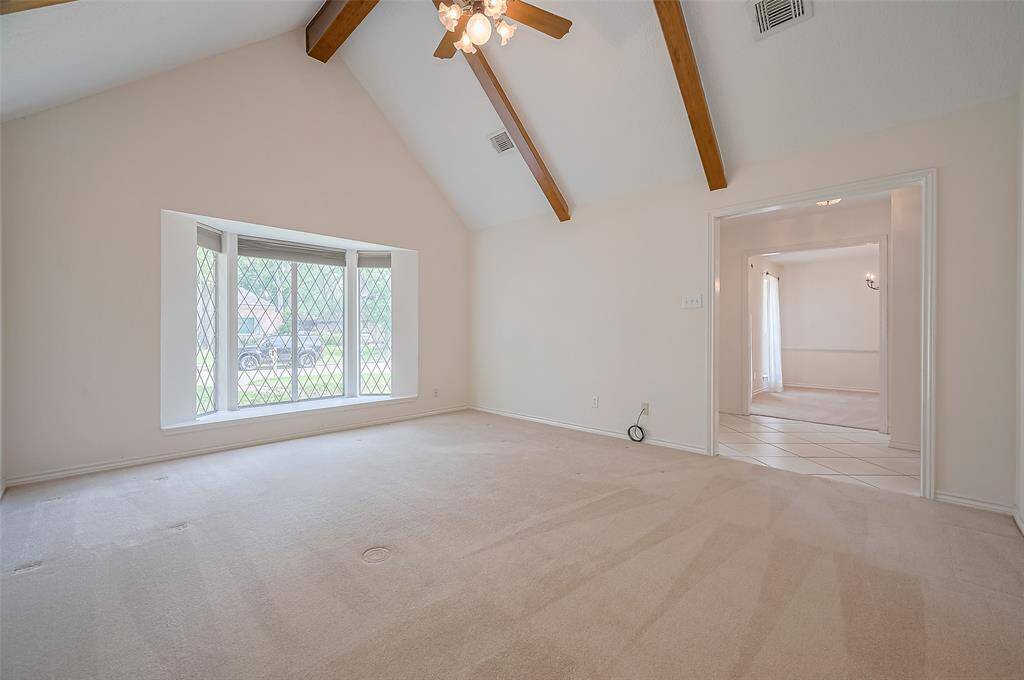 To the right of the foyer is a spacious formal living room (15.6 x 13.10) with a vaulted ceiling featuring wooden beams and a ceiling fan. This versatile room has endless possibilities, whether as a home office, children's game room, second TV room, man-cave, or more.